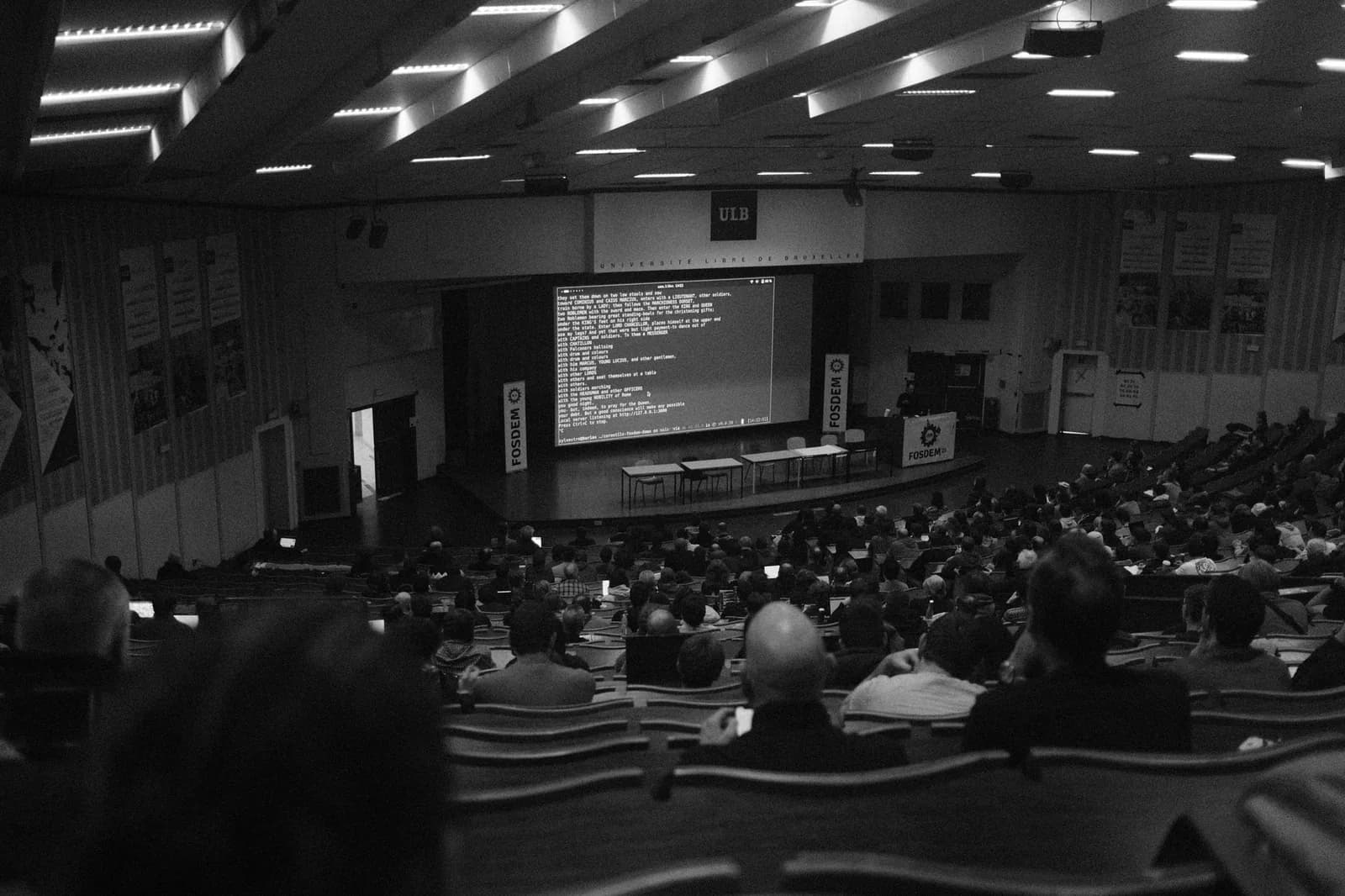 Amphithéâtre bondé de l'Université libre de Bruxelles, rangées d'étudiants face à un écran de projection