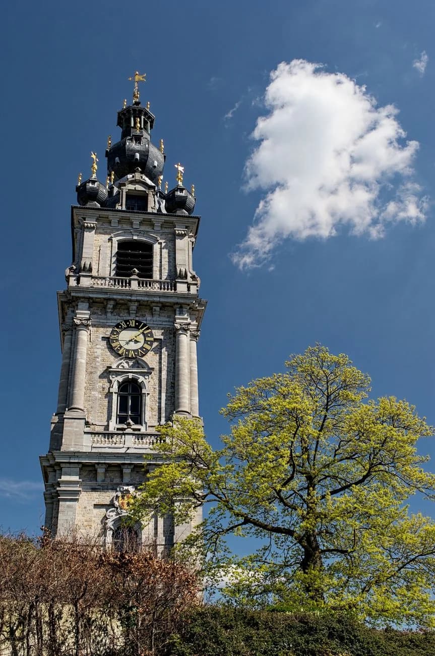 Le beffroi baroque de Mons, ses bulbes d'ardoise et ses ornements dorés sur un ciel bleu