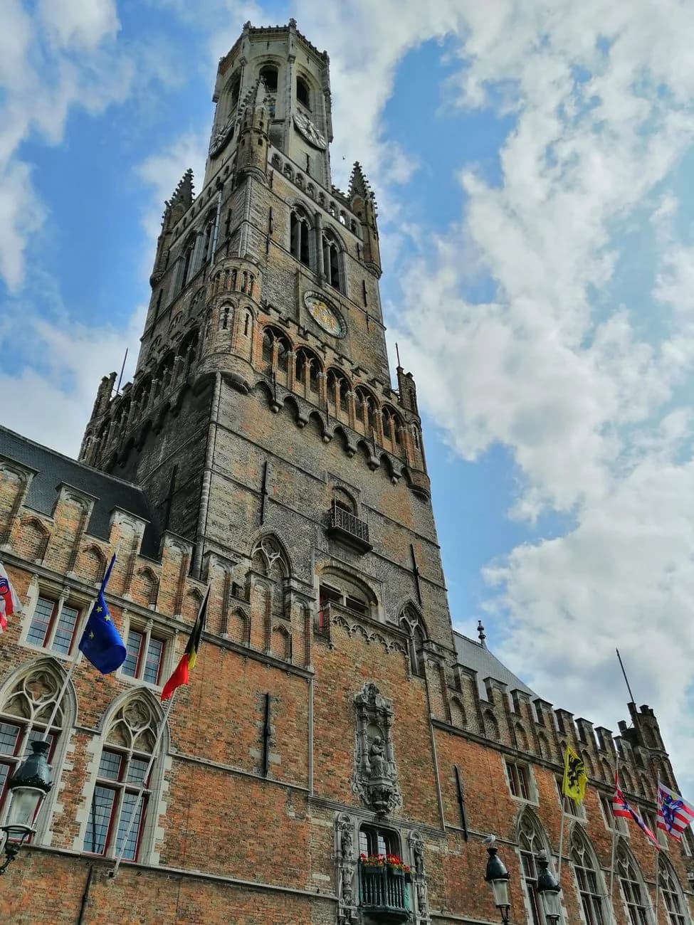 Le beffroi de Bruges vu en contre-plongée, avec les drapeaux flottant sur la façade des halles