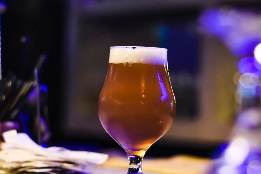 Verre tulipe de bière artisanale ambrée surmontée de mousse, posé sur le comptoir d'un bar