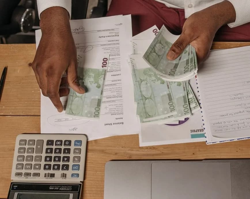 Billets de 100 euros comptés à la main sur un bureau, à côté d'une calculatrice et d'un ordinateur portable
