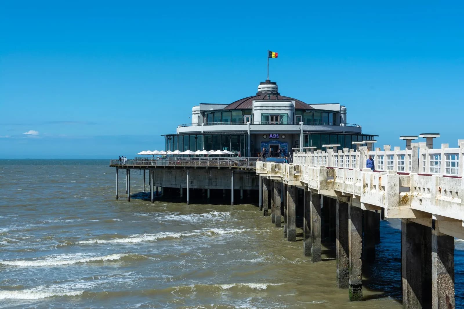 Rotonde vitrée du pier de Blankenberge posée sur pilotis au-dessus de la mer, drapeau belge au sommet