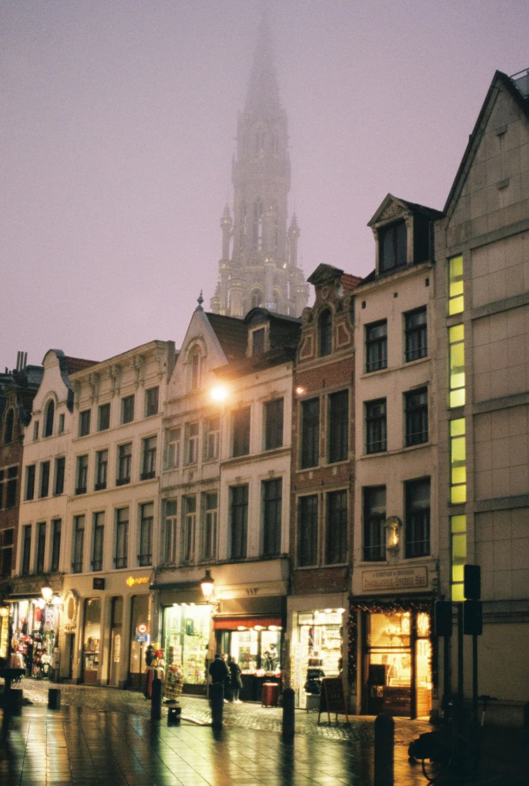Ruelle commerçante de Bruxelles sous la pluie, la tour de l'hôtel de ville dans la brume