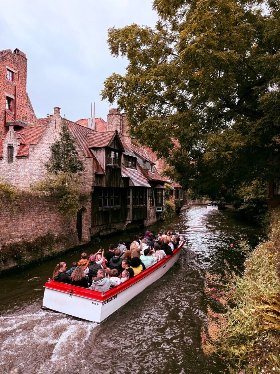 Bateau de promenade sur un canal étroit bordé de maisons en brique et d'une façade médiévale en bois