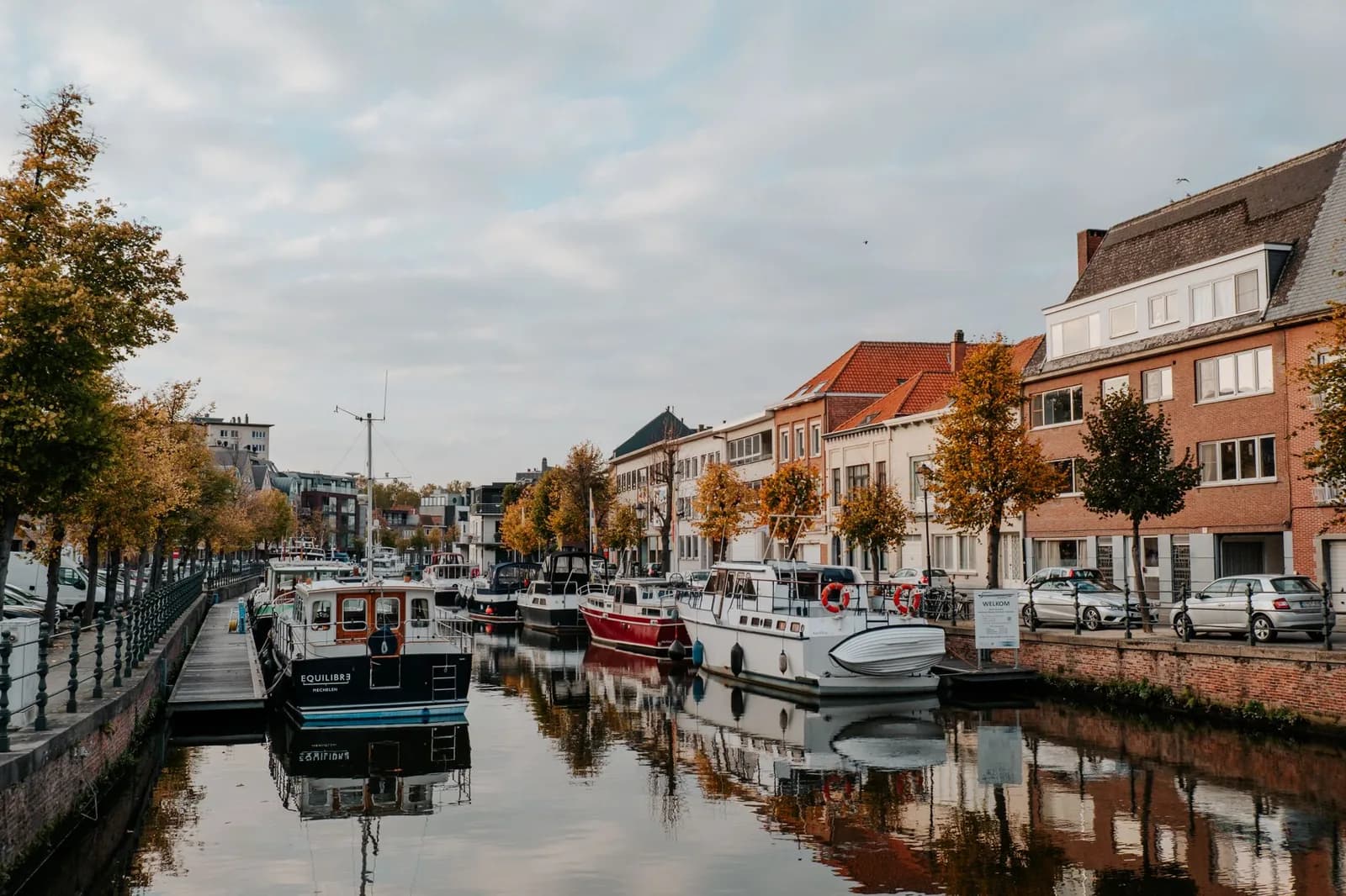 Bateaux amarrés le long d'un canal flamand bordé de maisons de brique et d'arbres en automne