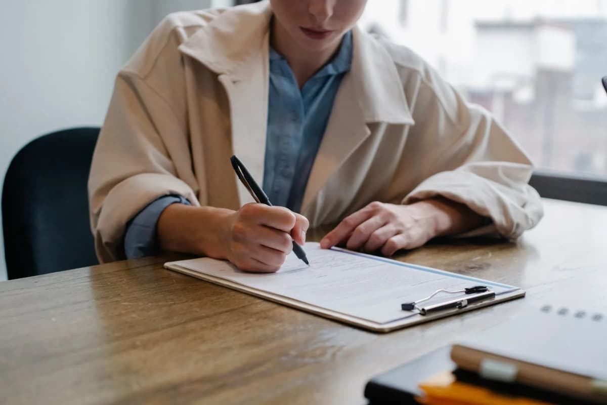 Une candidate remplit un formulaire sur une écritoire à pince, assise à un bureau