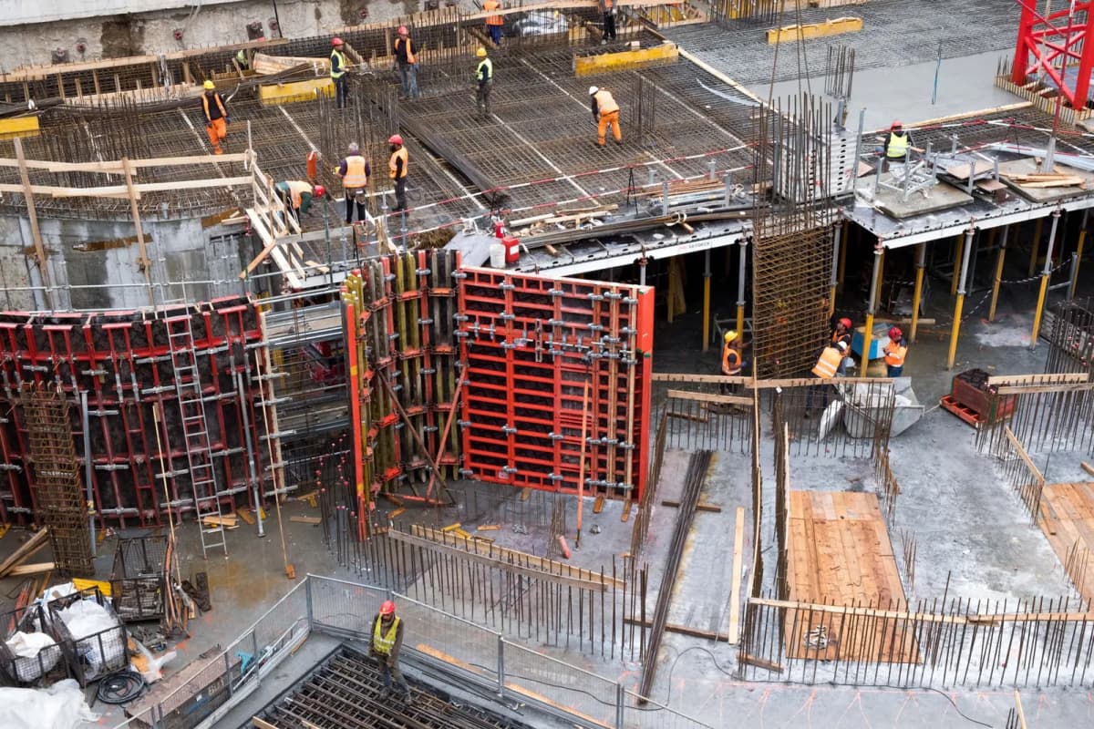 Ouvriers en gilet de sécurité sur un chantier de gros œuvre, entre coffrages rouges et ferraillage