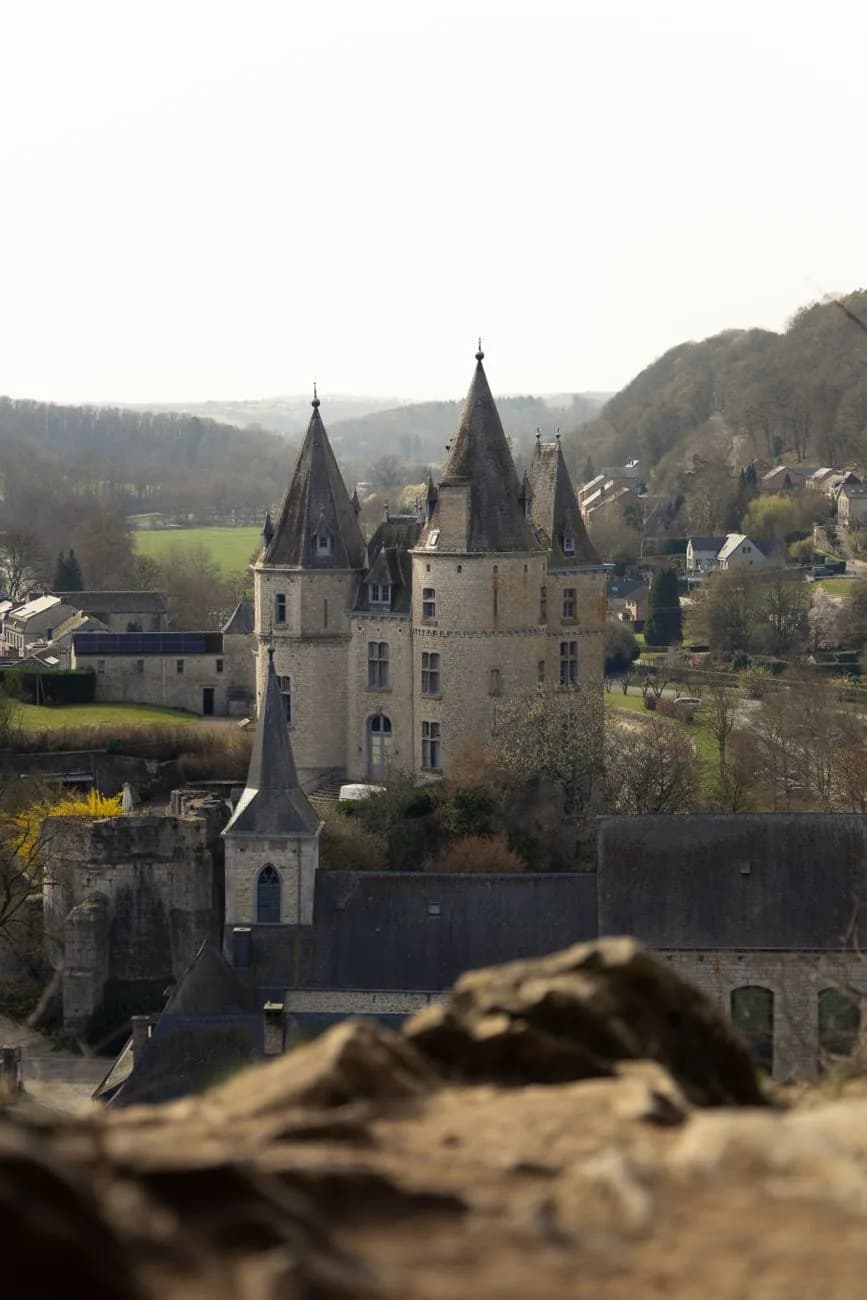 Château en pierre aux tours à toits coniques, au milieu d'un village serré entre des collines boisées