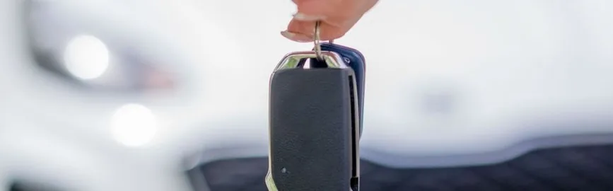 Une main tend la clé d'une voiture blanche garée derrière, remise d'une voiture de société