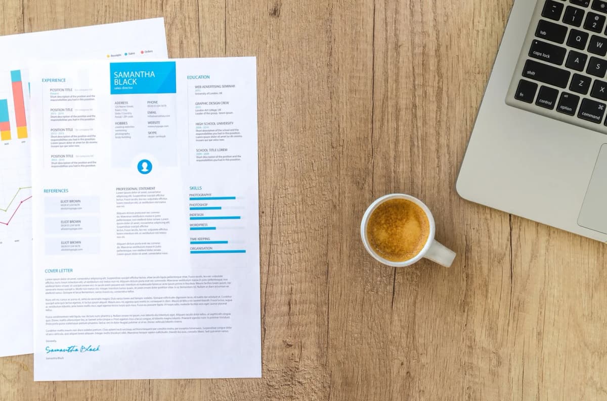 Un CV imprimé posé sur un bureau en bois, à côté d'une tasse de café et d'un ordinateur portable