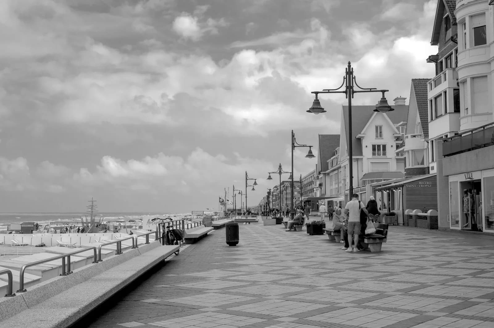 Promenade de digue carrelée bordée de lampadaires anciens et de villas à pignons, en noir et blanc