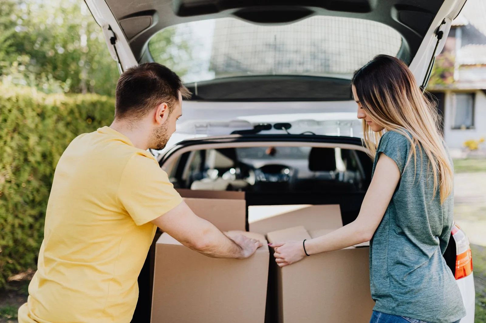 Un couple charge des cartons de déménagement dans le coffre d'une voiture blanche