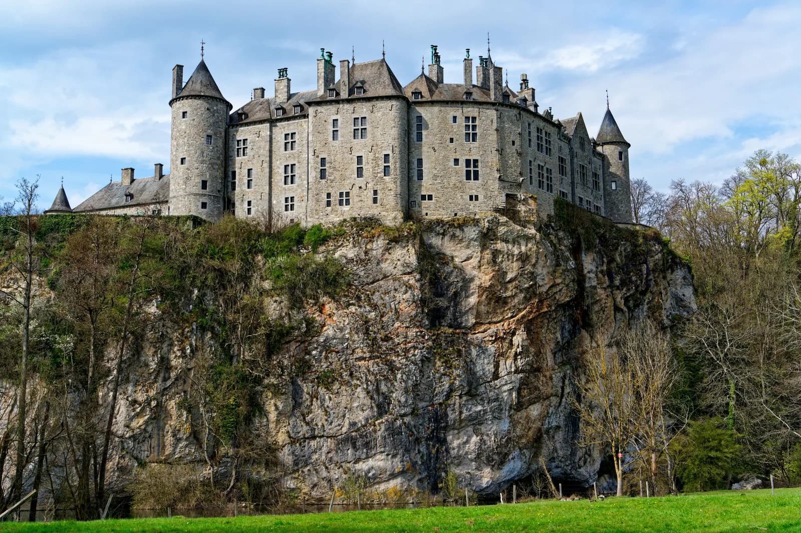 Le château de Walzin et ses tours rondes en pierre grise, posés au bord d'une haute falaise calcaire boisée