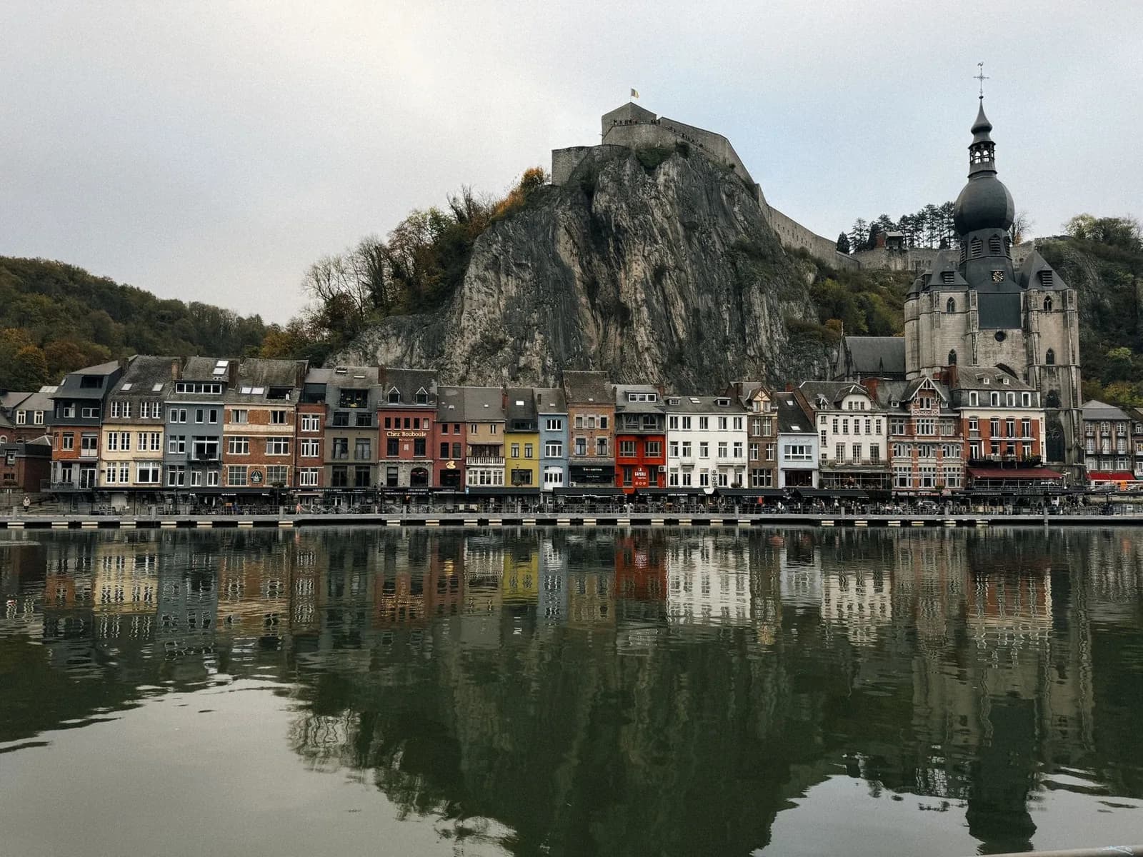 Les façades colorées du quai de Dinant alignées au bord de la Meuse, sous le rocher de la citadelle, reflétées dans l'eau