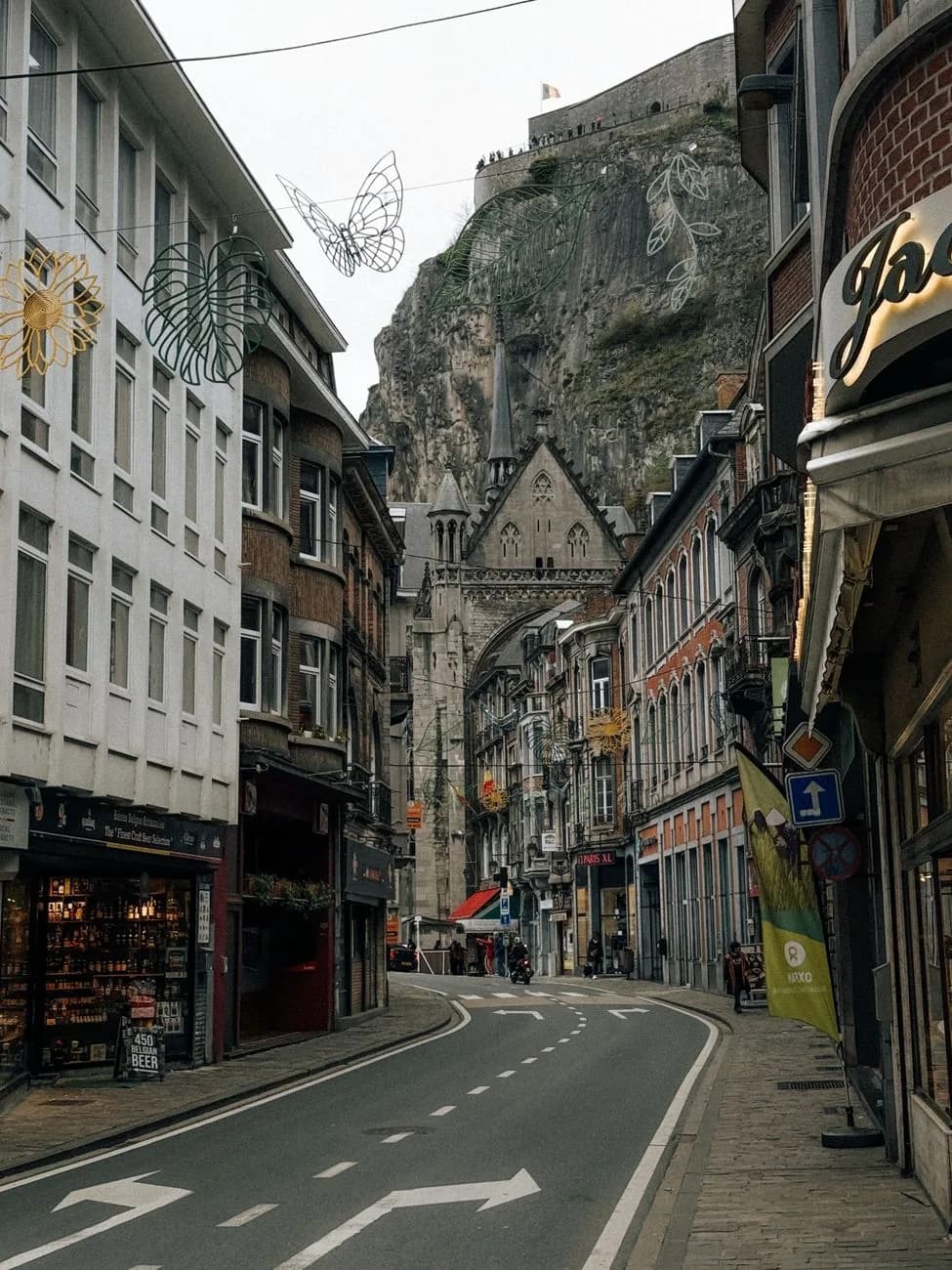 Rue commerçante de Dinant menant vers la collégiale, avec les remparts de la citadelle au sommet de la falaise en arrière-plan