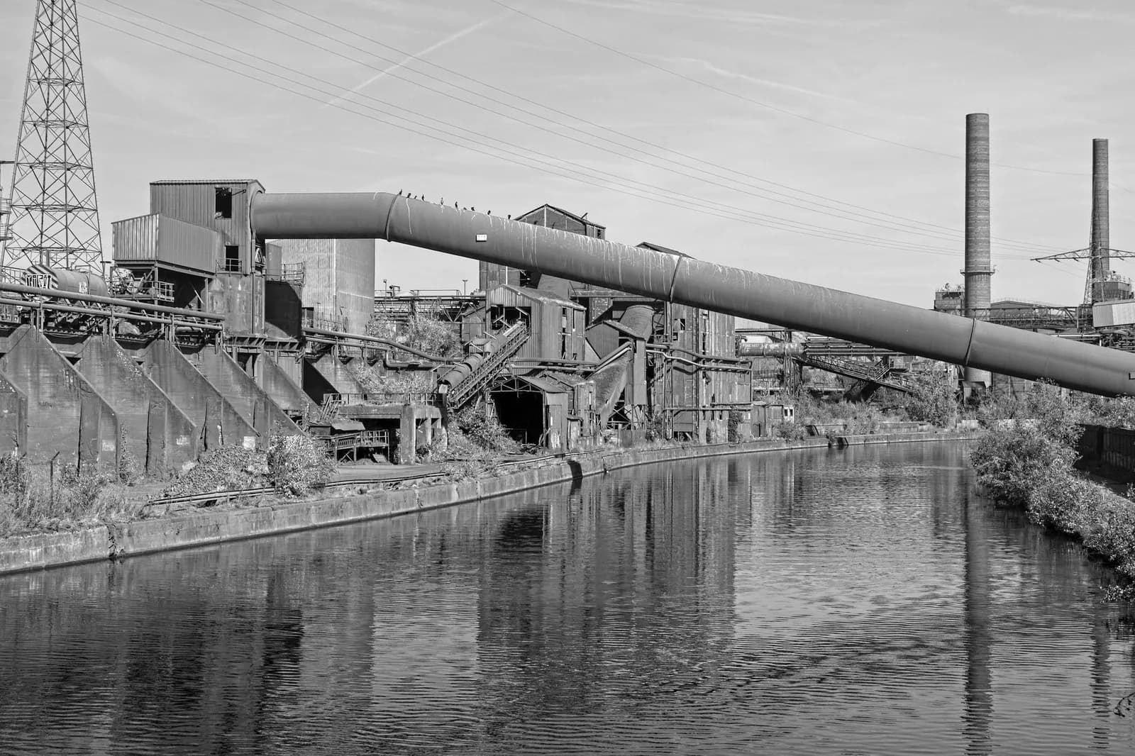 Ancienne installation sidérurgique et ses cheminées le long d'un canal à Charleroi, en noir et blanc