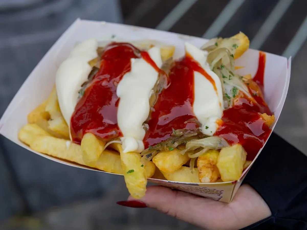 Cornet de frites belges nappé de ketchup et de mayonnaise, tenu à la main