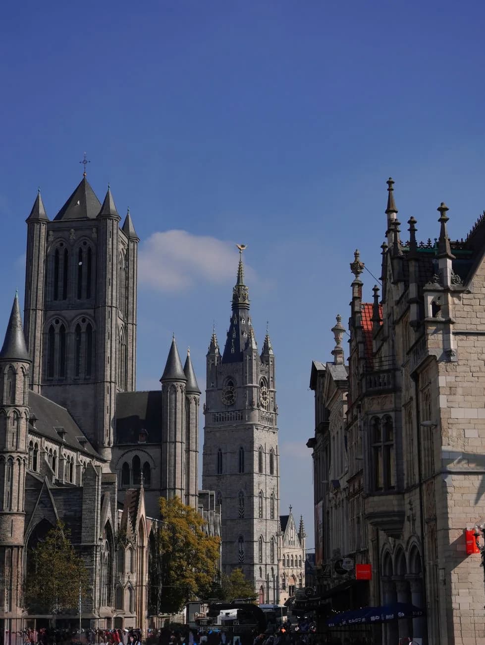 La tour de l'église Saint-Nicolas et le beffroi de Gand alignés au-dessus des façades du Korenmarkt