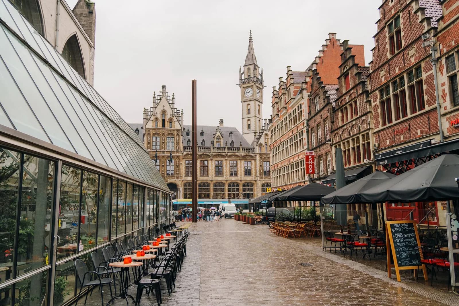 Terrasses installées sur les pavés du Groentenmarkt à Gand, le long de la verrière du Groot Vleeshuis, avec la tour horloge de l'ancienne poste au fond