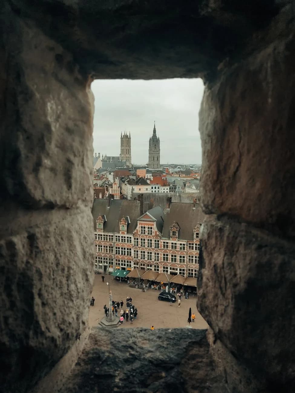 Vue à travers un créneau du château des Comtes sur une place de Gand et, au loin, les tours de la cathédrale et du beffroi