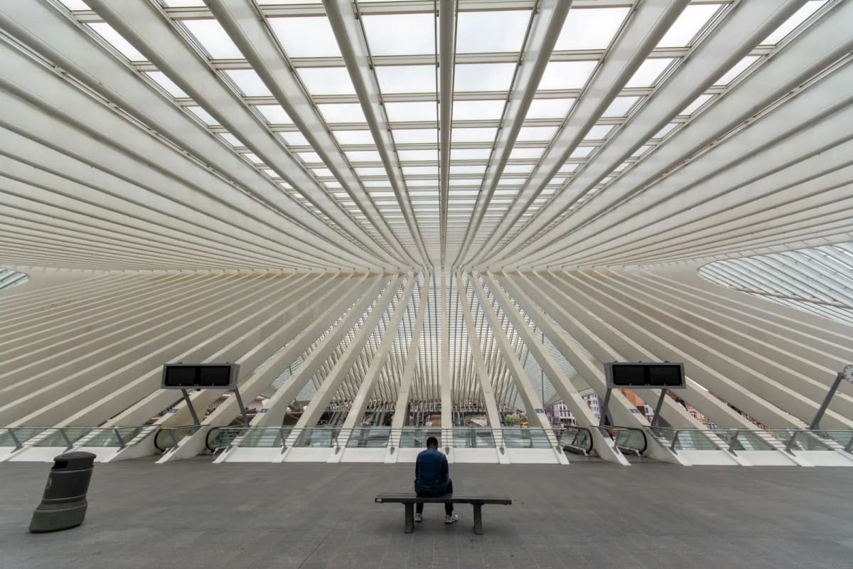 Une personne assise sur un banc sous la voûte nervurée du hall de la gare de Liège-Guillemins