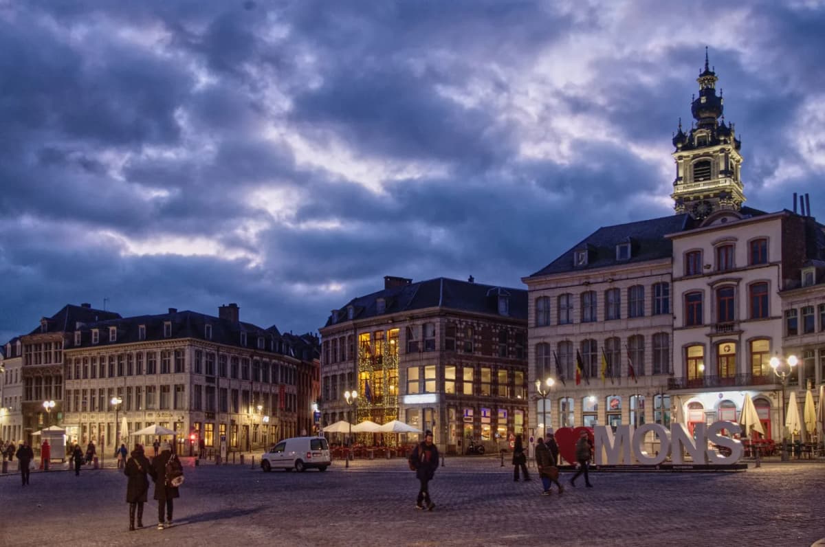 La Grand-Place de Mons au crépuscule, les lettres géantes MONS et le beffroi éclairé au-dessus des toits