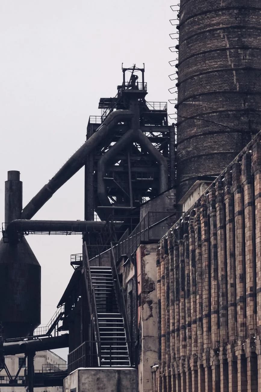 Haut-fourneau désaffecté, ses grandes conduites courbes et ses escaliers métalliques devant un mur de briques