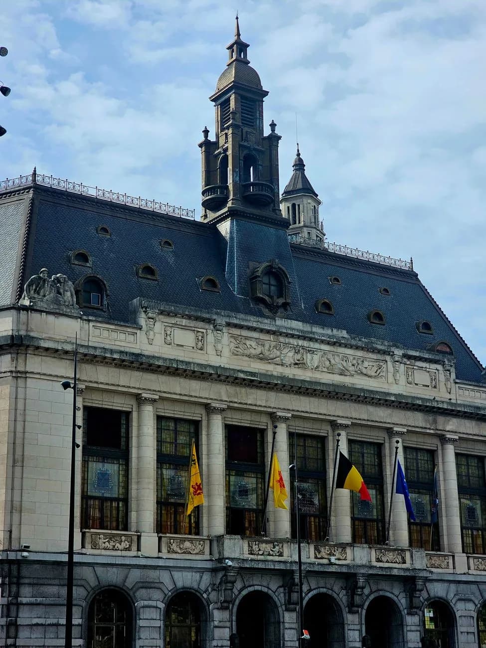 Façade monumentale d'un hôtel de ville wallon, sa frise sculptée et son campanile, pavoisée de drapeaux au coq hardi