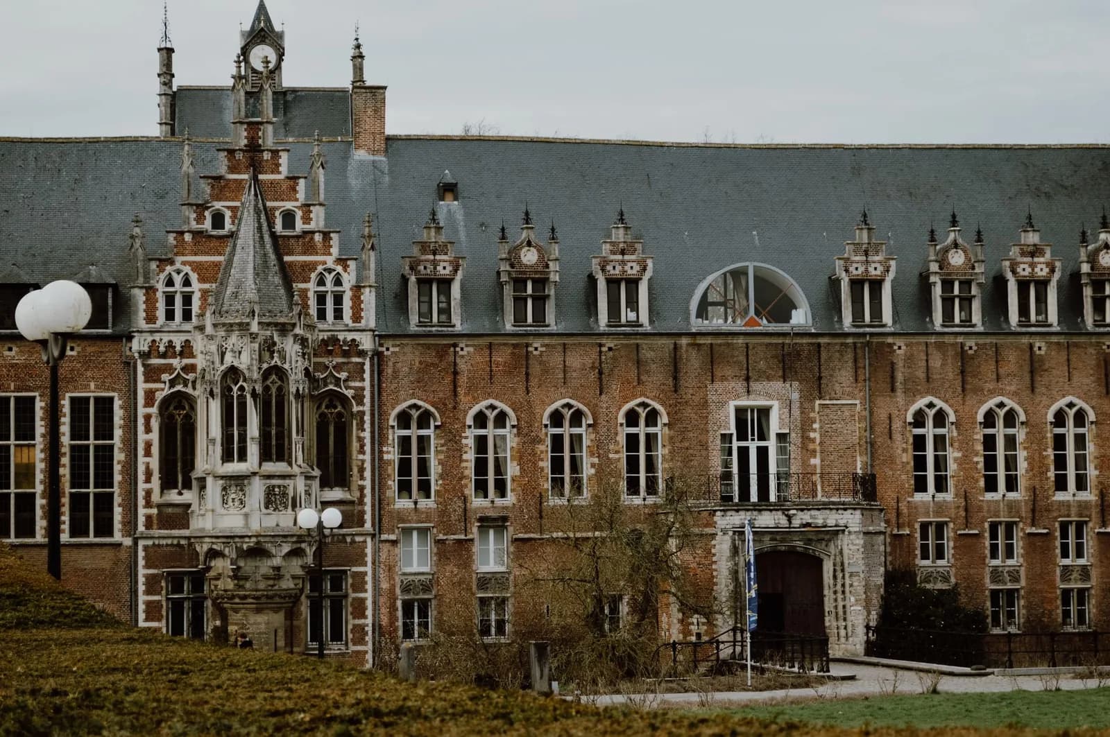 La façade en brique du château d'Arenberg à Heverlee, son oriel de pierre sculptée et son pignon à horloge, devant une pelouse