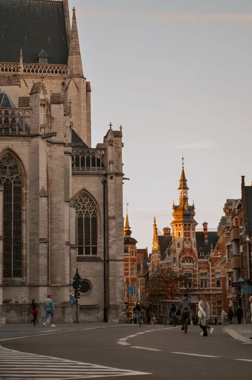 Le flanc en pierre de l'église Saint-Pierre de Louvain au soleil couchant, avec la tour néogothique de l'ancienne poste au fond de la rue