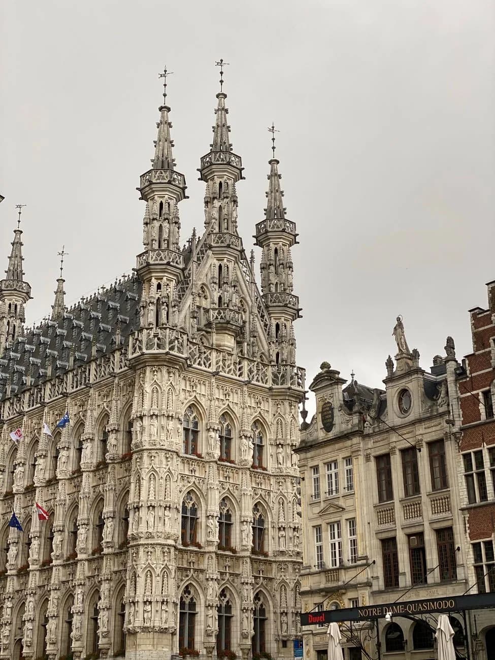 La façade de pierre blanche de l'hôtel de ville de Louvain, couverte de statues et de trois tourelles ajourées, vue depuis la Grand-Place