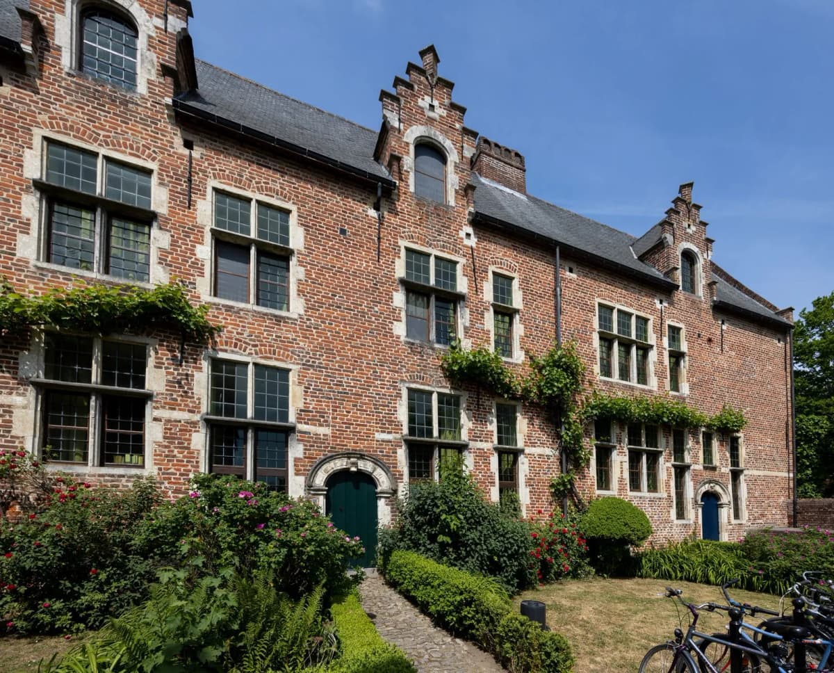 Maisons anciennes en brique rouge et pierre blanche à pignons à redents, bordées de jardinets fleuris et de vélos
