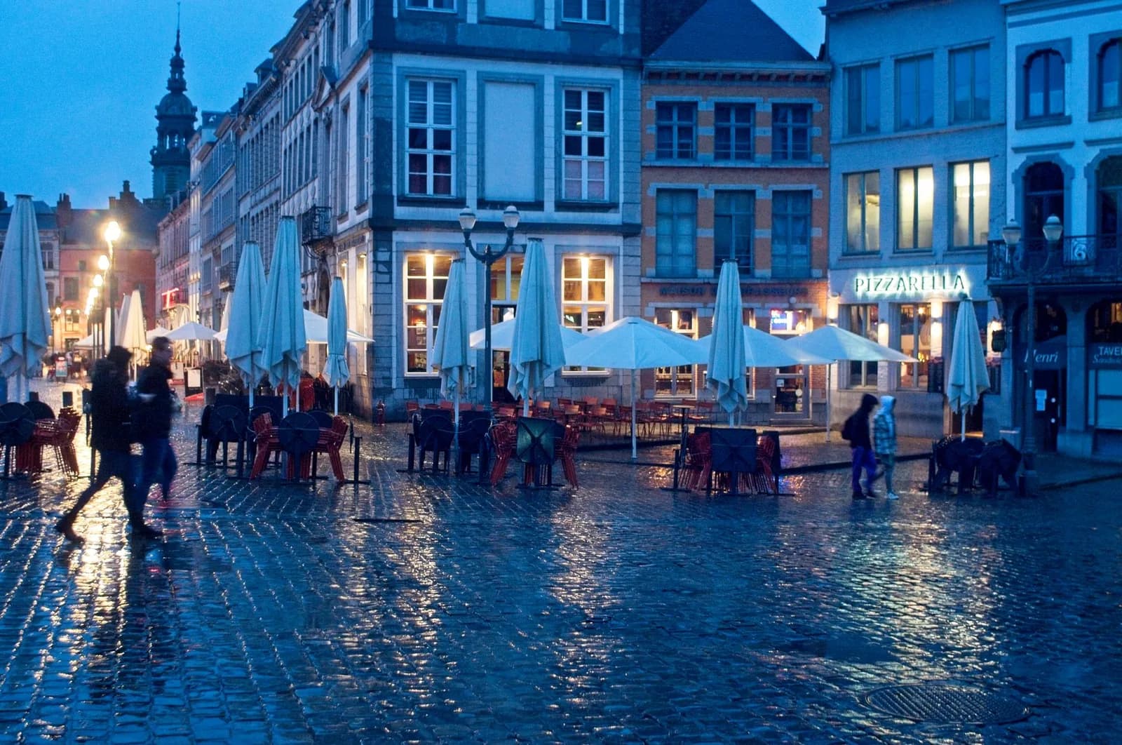 Pavés mouillés et terrasses de la Grand-Place de Mons à l'heure bleue, le beffroi au loin