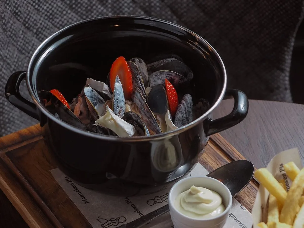 Casserole noire entière de moules à la sauce crémeuse, avec une coupelle de mayonnaise et un cornet de frites sur une planche en bois