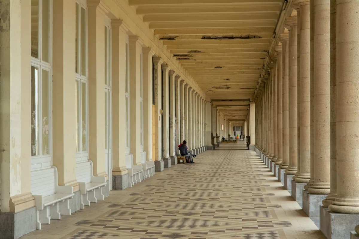 Longue colonnade des Galeries royales d'Ostende, sol carrelé à motifs, bancs blancs et un couple assis au loin