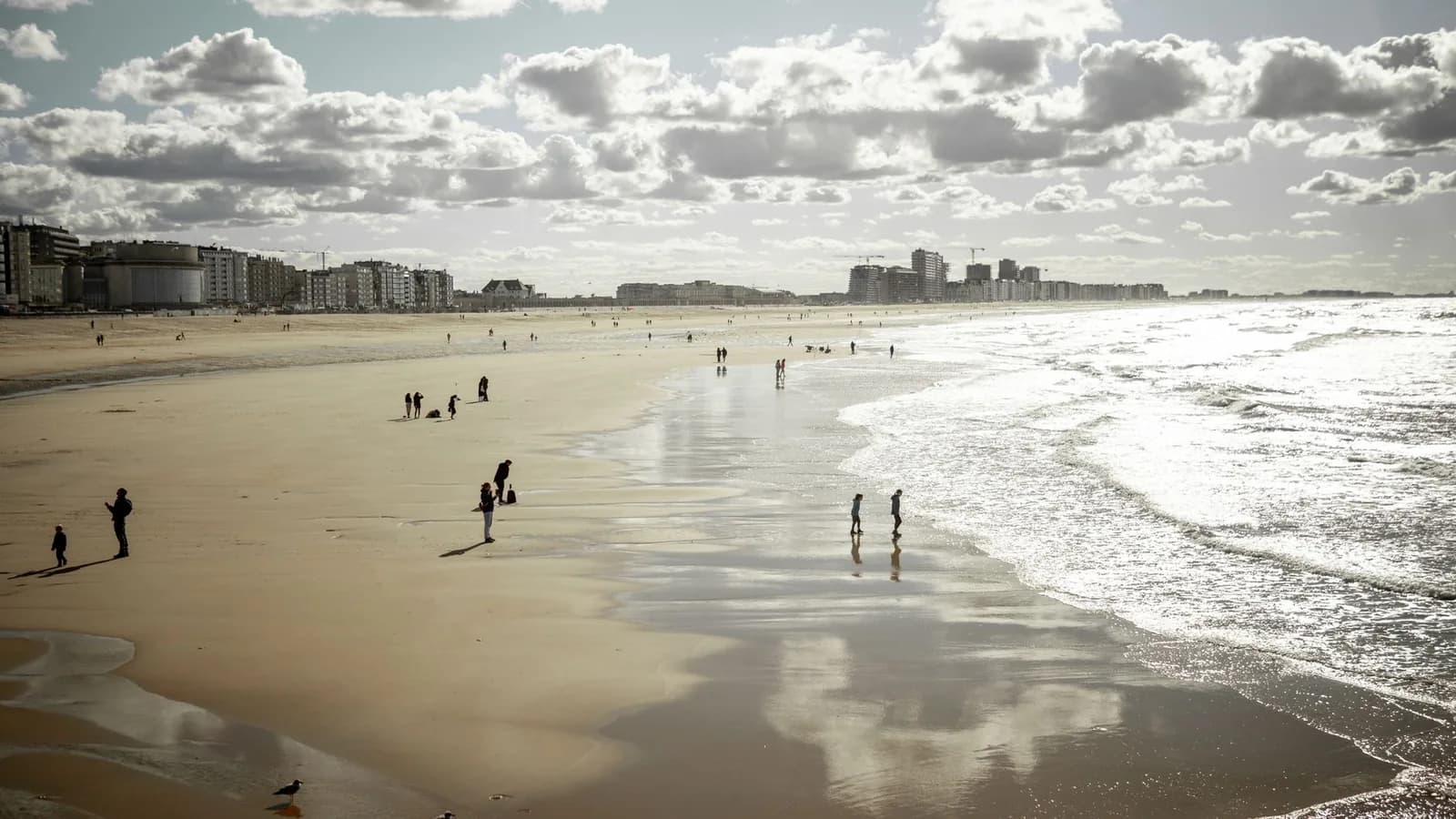 Grande plage de sable d'Ostende à marée descendante, promeneurs au bord de l'eau et front de mer bâti jusqu'au Kursaal sous un ciel nuageux