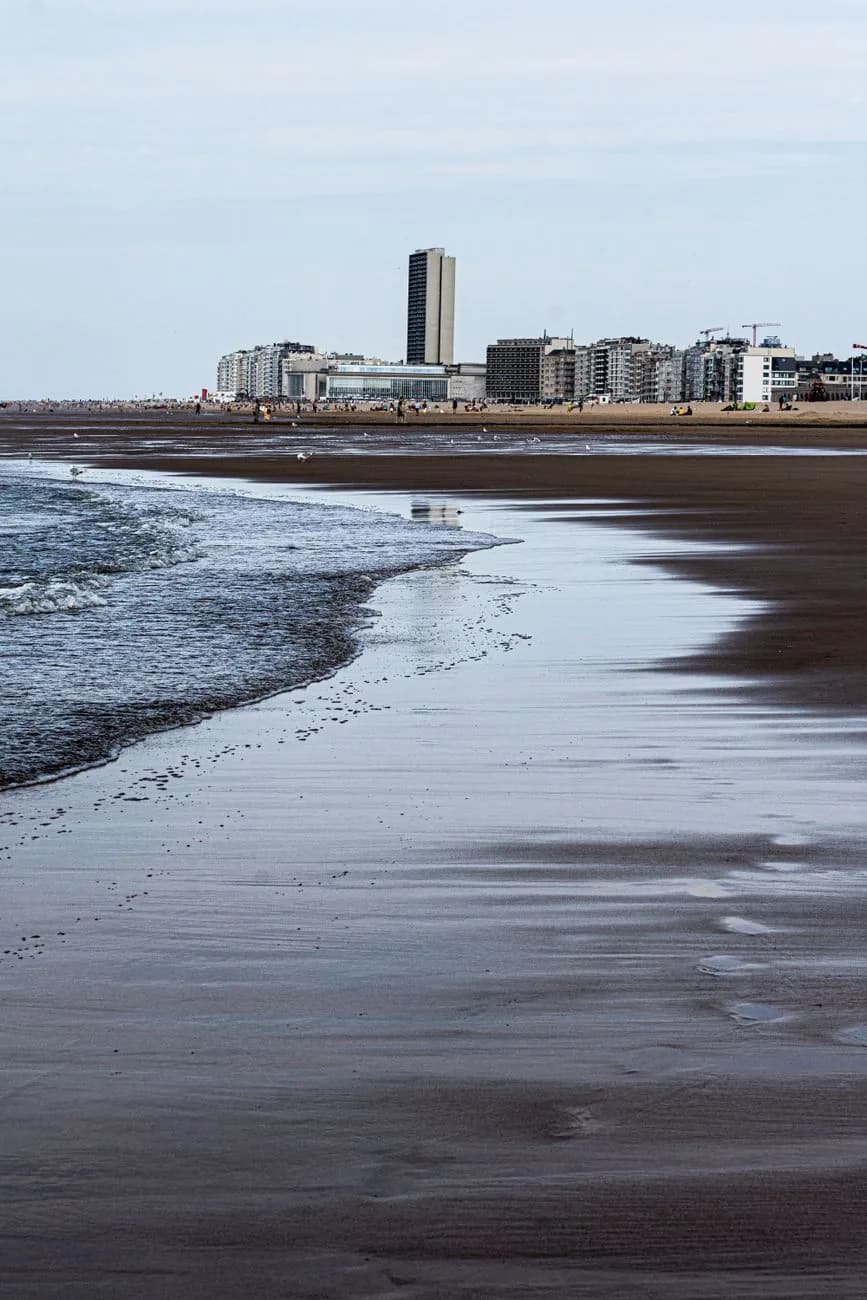Plage à marée basse, sable humide et vagues au premier plan, front de mer d'immeubles à l'horizon