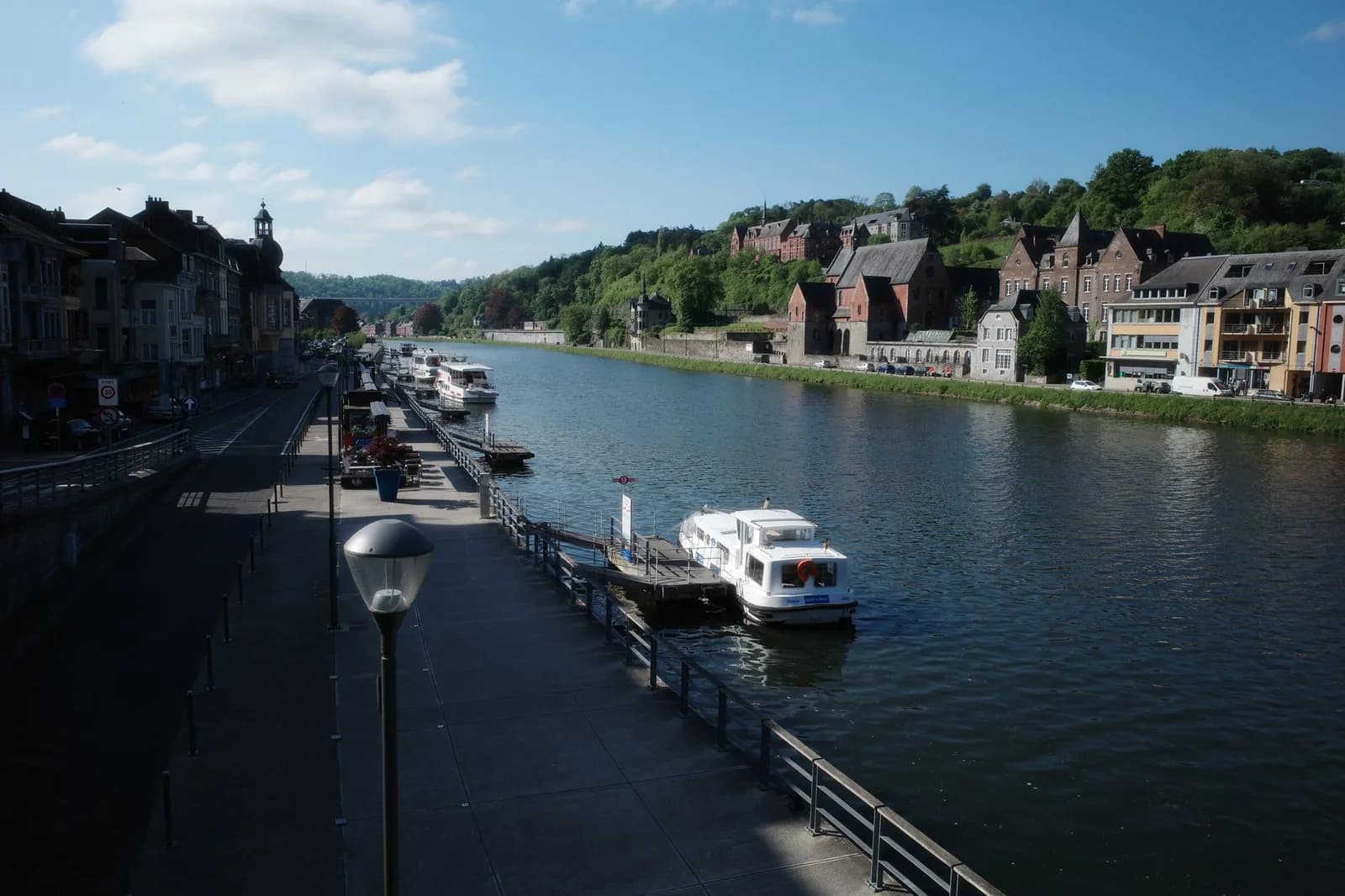 Bateaux de plaisance amarrés le long d'un quai fluvial, promenade et coteau boisé en face