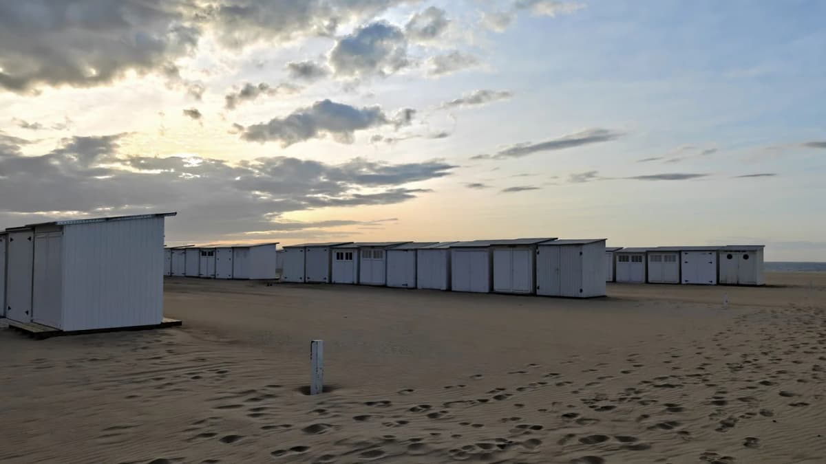Longue rangée de cabines de plage blanches alignées sur le sable au crépuscule