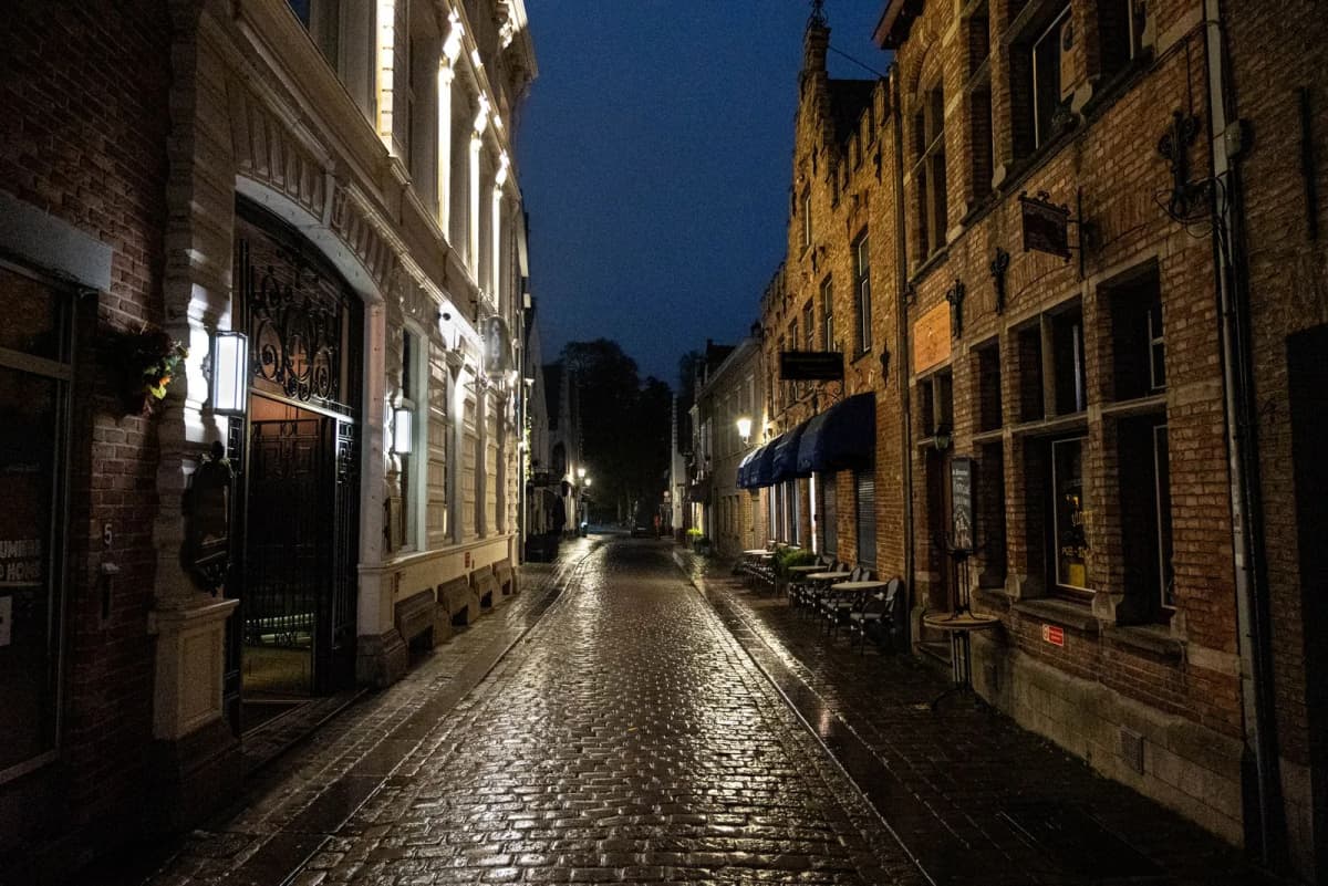Rue pavée déserte et luisante de pluie à la tombée de la nuit, bordée de maisons anciennes éclairées