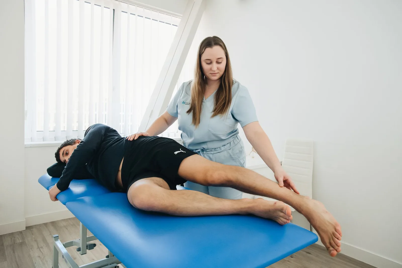 Une kinésithérapeute étire la jambe d'un patient allongé sur une table de soin