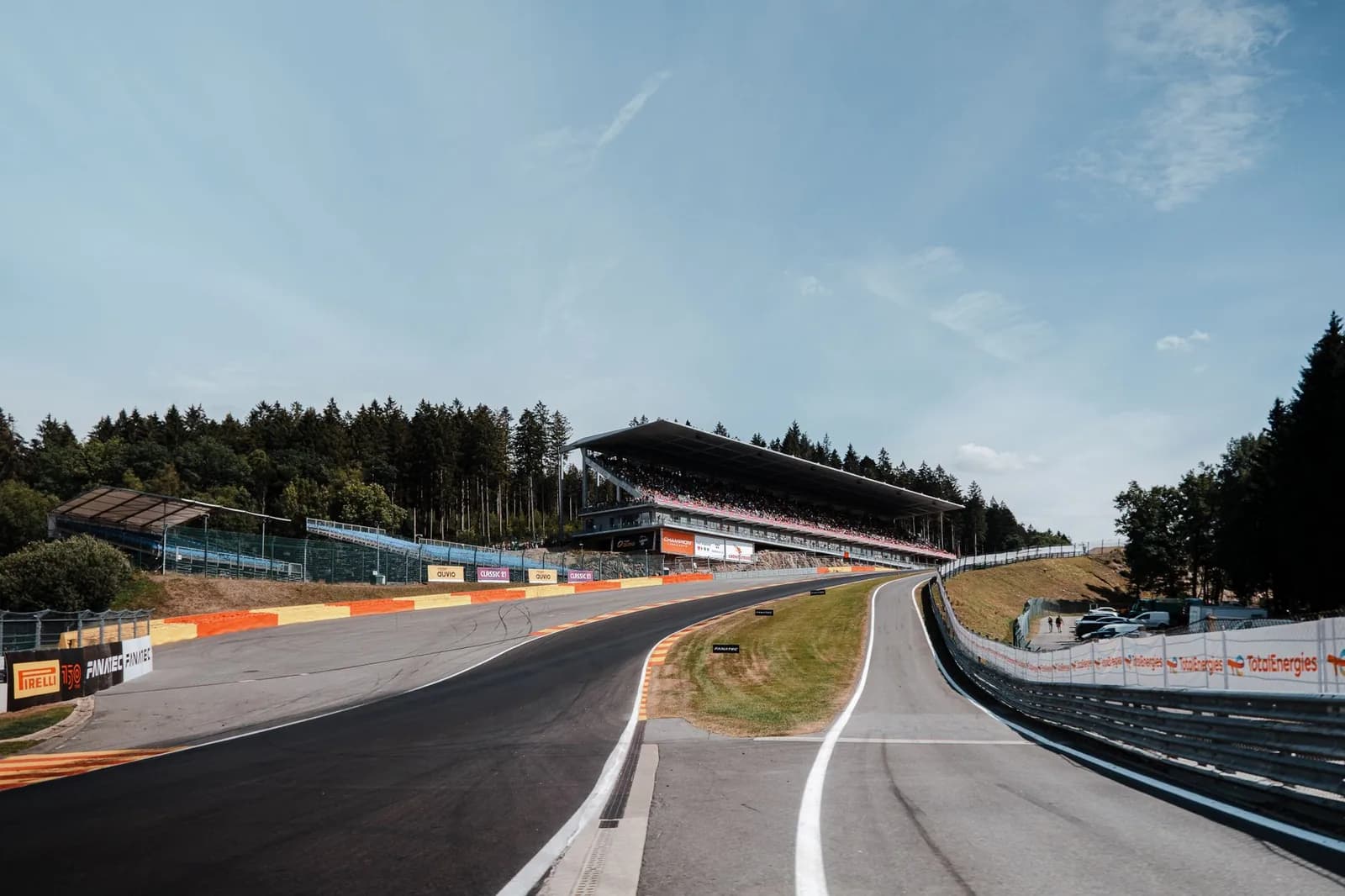 Piste montante du circuit de Spa-Francorchamps, vibreurs rouge et jaune et grande tribune bordée de sapins